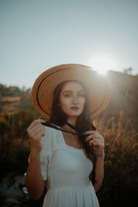 Portrait of young woman wearing hat standing against sky