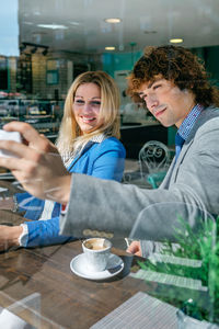 Business people taking selfie while sitting in cafe seen through window