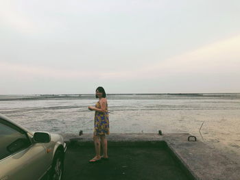 Woman standing on sea against sky during sunset