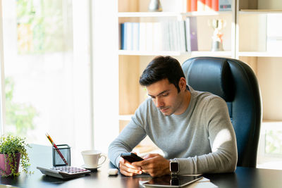 Young man using mobile phone while sitting on table