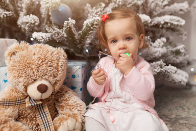 Portrait of cute girl sitting by teddy bear against christmas tree at home