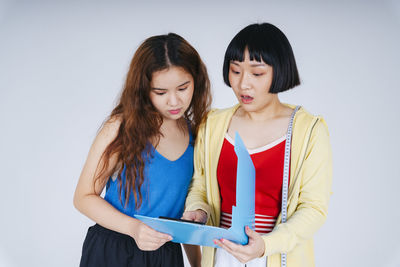 Smiling lesbian couple looking at file against gray background