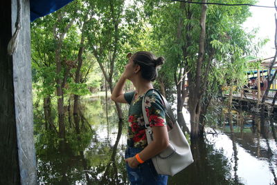 Young woman standing by lake against trees