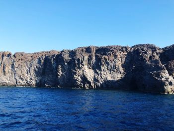 Rock formations by sea against clear blue sky