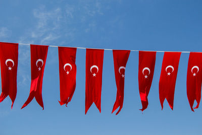 Low angle view of red flags hanging against blue sky