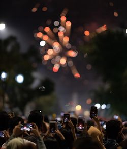 Group of people photographing firework display at night