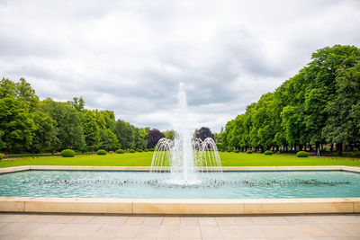 Fountain in park by lake against sky