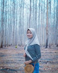 Woman standing by tree trunk in forest