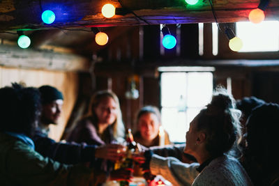 Happy male and friends toasting drinks while sitting in cottage