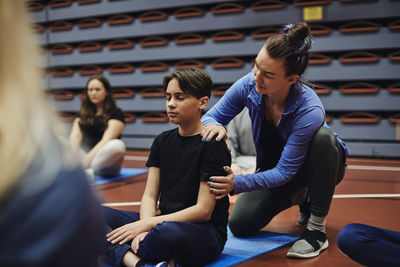 Female coach guiding male student sitting with eyes closed in sports court