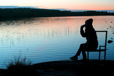 Silhouette woman sitting by lake during sunset