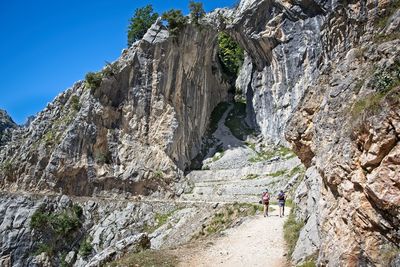 Man standing on cliff by mountain against sky