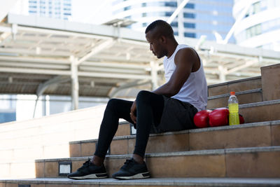 Contemplating man sitting on staircase with boxing gloves and drink