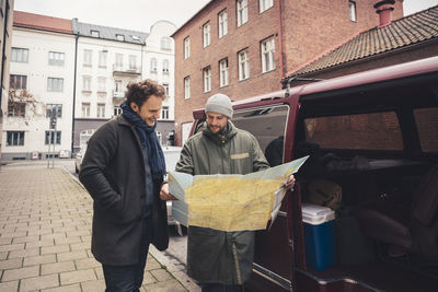 Smiling man examining map with male friend on footpath