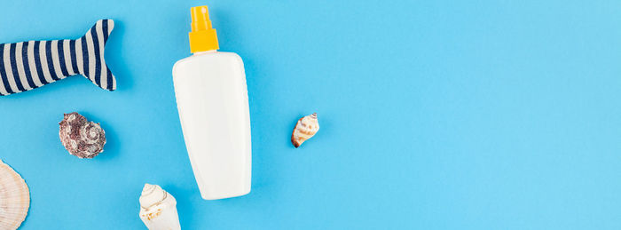 Close-up of suntan lotion bottle and seashells against blue background