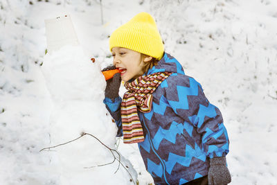 Boy biting snowman nose during winter
