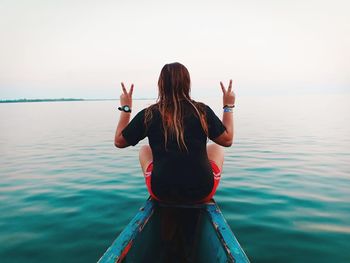 Rear view of woman with arms raised in sea against sky