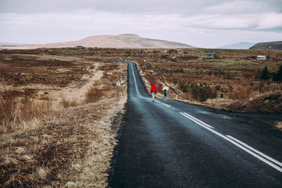 Rear view of couple skateboarding on road against landscape