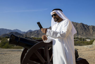 Man using phone while standing by cannon against sky