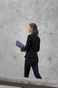 Side view of woman standing with folders against wall