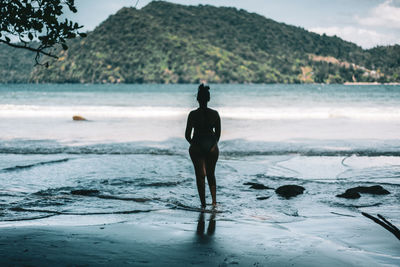 Rear view of woman standing at beach against sky