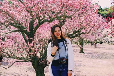 Portrait of young woman with pink flowers against tree