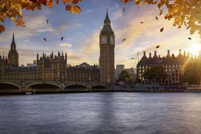 Buildings by river against sky at sunset