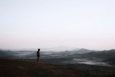 Rear view of man standing on mountain against sky