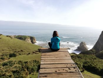 Rear view of woman looking at seascape while sitting on boardwalk