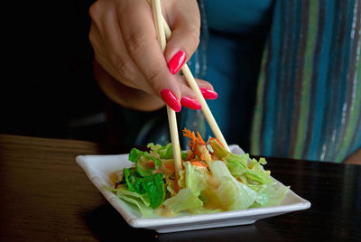 Cropped hand of woman having salad at table