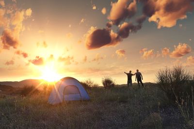 People standing on field by tent against sky during sunset