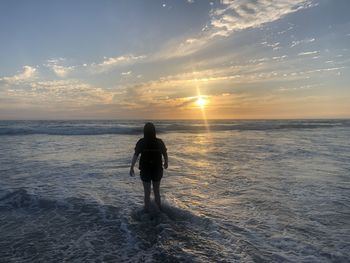 Rear view of man standing on beach during sunset