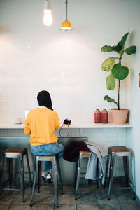 Full length rear view of female blogger sitting on stool at cafe