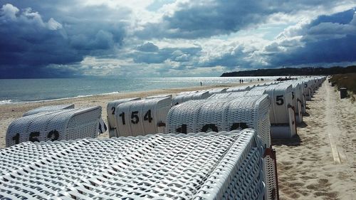 Row of hooded chairs at beach against cloudy sky