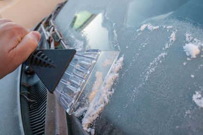 Cropped hand removing snow on car windshield