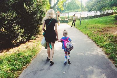 Rear view of mother and daughter walking on road