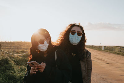 Portrait of woman wearing mask with friend against sky