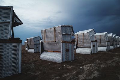 Hooded beach chairs on sand against cloudy sky