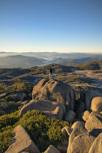 Rear view of man standing on rock against sky