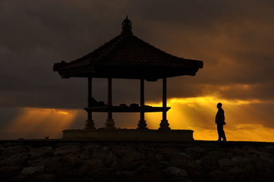 Silhouette man standing by gazebo against cloudy sky during sunset