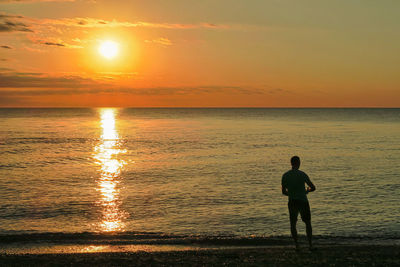 Silhouette man standing on beach against sky during sunset