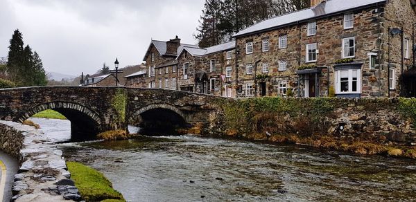 Arch bridge over river amidst buildings against sky