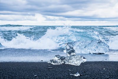 Iceberg chunk on black sand with waves rushing in background at diamond beach
