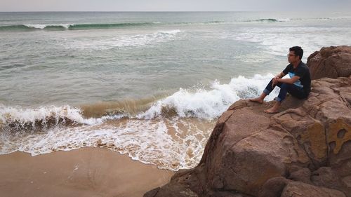 Man sitting on rock at beach