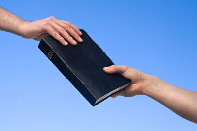 Cropped hands of man holding bible against clear sky