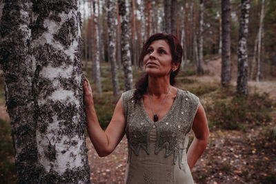 Portrait of a young woman standing by tree trunk in forest