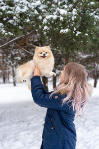 Young woman carrying dog while standing in snow during winter