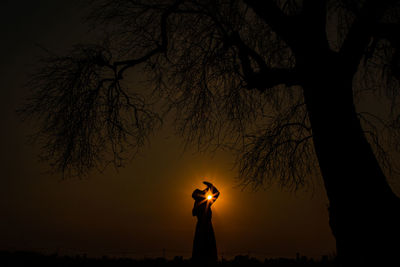 Silhouette man standing by tree against sky during sunset