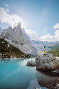 Woman standing on rock by lake against sky