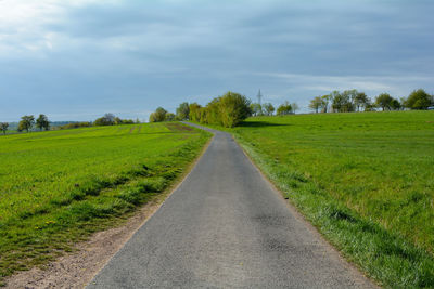 Empty road amidst field against sky